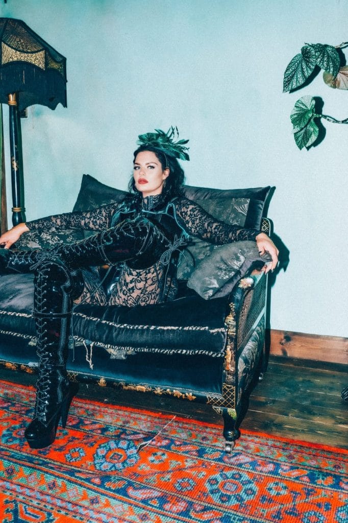 Mistress Charlotte reclining on a black leather sofa in lace and thigh-high boots