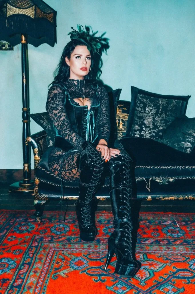 Mistress Charlotte, professional dominatrix, seated on a sofa in lace and leather boots