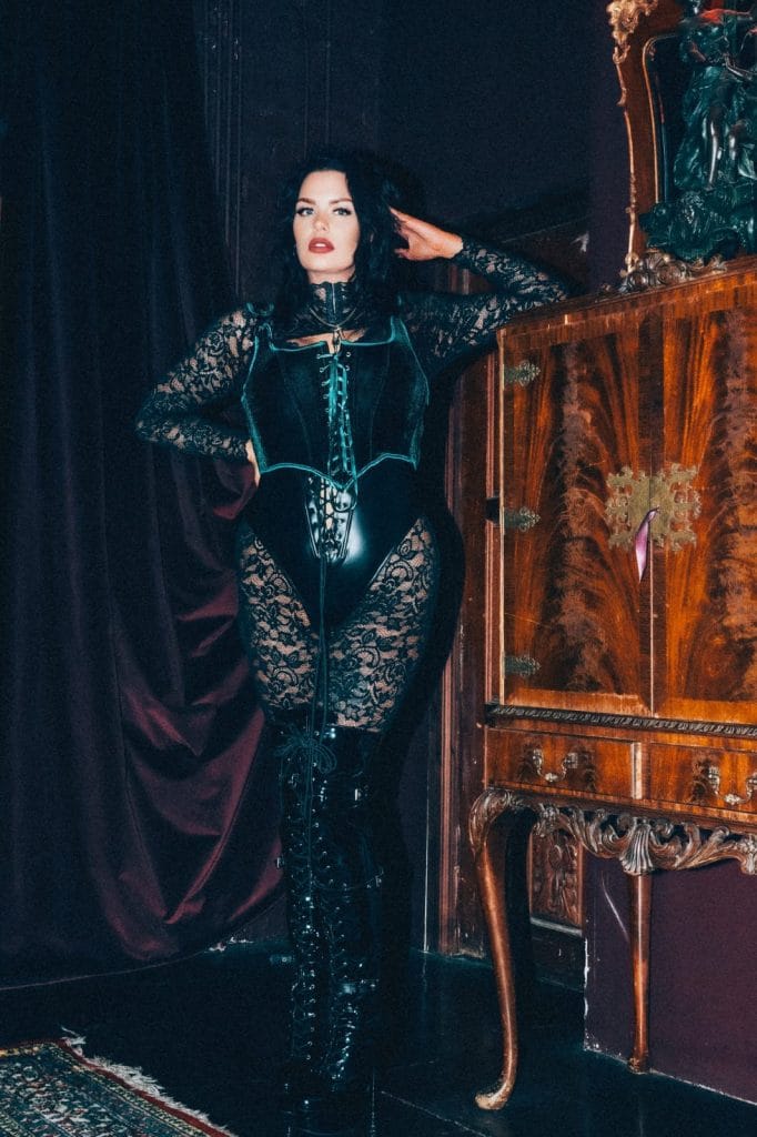Mistress Charlotte standing beside an antique cabinet, chastity keyholder in London