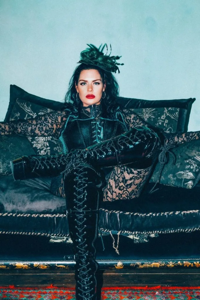 London dominatrix Mistress Charlotte seated on a black velvet sofa in lace and lace-up boots