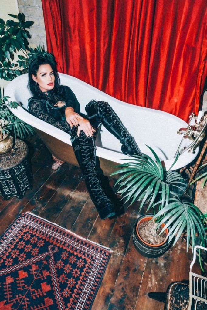 Mistress Charlotte in black lace and latex boots, reclining in a clawfoot bath