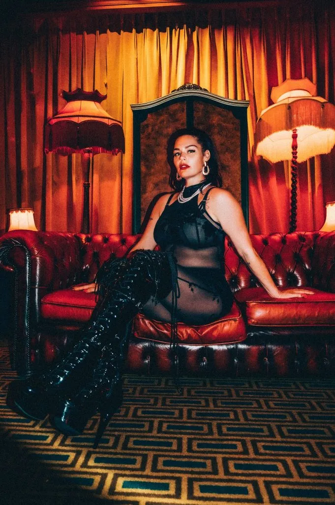 Mistress Charlotte enthroned on a red Chesterfield sofa in thigh-high boots